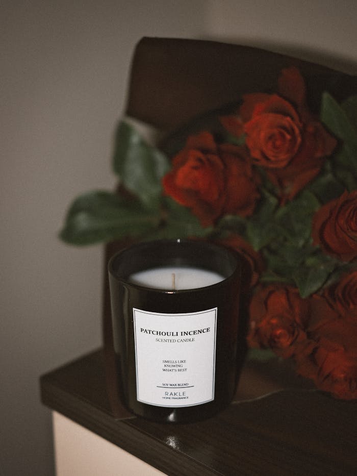 Black candle beside a bouquet of red roses on a wooden surface, creating a warm ambiance.